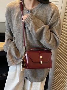 Chic burgundy leather crossbody bag with gold buckle and wooden bead charm accessory