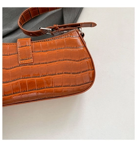 Detail of orange-brown faux crocodile skin texture and silver buckle on the shoulder bag