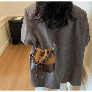 Detail of a brown suede drawstring bucket bag with twisted handle and CAEKYI branding