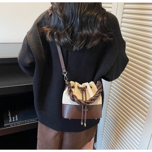 Detail of a brown and cream drawstring bucket bag with woven handle and leather strap