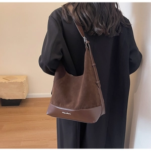 Detail view of a large brown suede tote bag worn on shoulder by a model in soft light