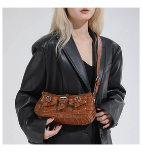 Detail of brown crocodile embossed bag with silver buckles worn by model in black leather jacket