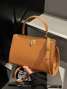 Minimalist brown leather tote bag with gold twist lock on a modern urban background