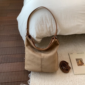 Flat lay of large brown suede hobo bag with adjustable strap on wooden floor