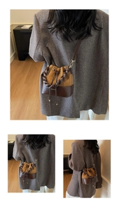 Detail of a brown leather bucket bag with a twisted handle and gold logo lettering