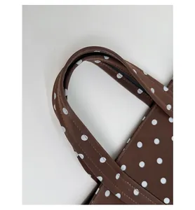 Detail of brown polka dot tote bag showing dual handles and reinforced stitching