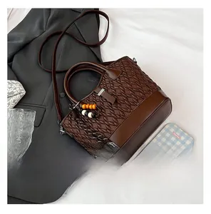 Detail of woven brown leather handbag with wooden bead charm and crossbody strap