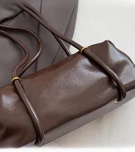 Detail of dark brown cylinder shoulder bag featuring glossy PU leather and gold metal rings
