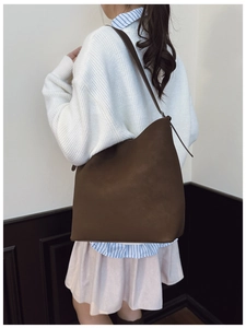 Detailed view of deep brown matte leather tote bag worn by model in minimalist indoor setting