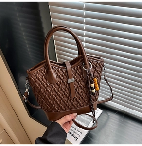 Detailed close-up of brown woven texture handbag with detachable strap and colorful charm
