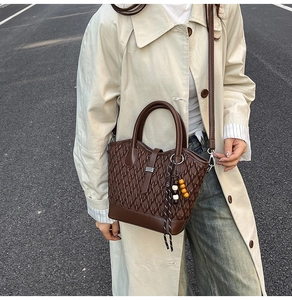 Detail of dark brown woven leather tote bag with colorful bead charm on the side