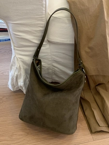 Retro olive green suede tote bag with adjustable strap on a minimalist sofa