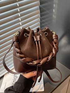 Brown bucket bag with woven handle and drawstring closure in warm lifestyle lighting