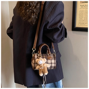 Detail of plaid Boston bag with leather straps and a plush bear charm worn with a blazer