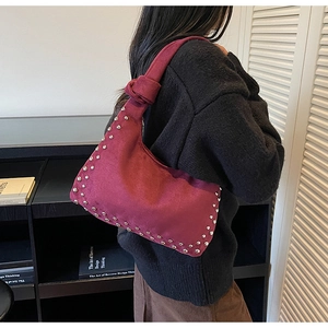 Detail of burgundy suede shoulder bag featuring silver rivets and knotted handle detail