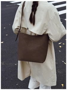 Rear view of model wearing a large dark brown matte leather bucket bag on street