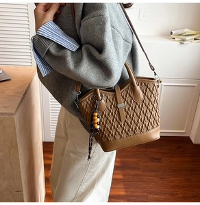 Brown tote bag with diamond woven pattern and wooden bead charm worn by a model