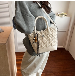Quilted cream crossbody bag detail with metallic handle and wooden beaded tassel charm