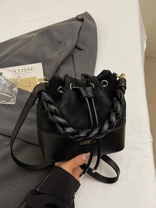Chic black bucket bag in mixed leather with woven handle on a stylish blazer background