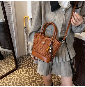 Detail of brown woven faux leather handbag with wooden bead charm and adjustable strap