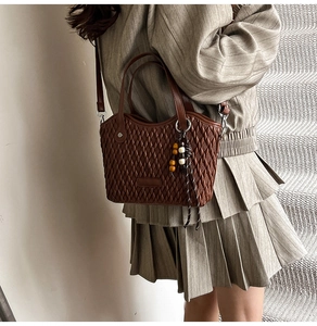 Brown woven bucket bag featuring wooden bead charm detail and stylish lattice texture