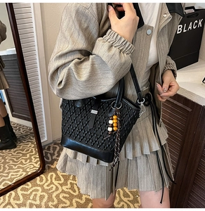 Detail of black woven texture handbag with colorful bead tassel and smooth leather handle