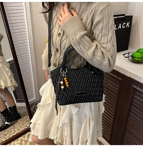 Close-up of black quilted bucket bag with woven texture and decorative wooden beads