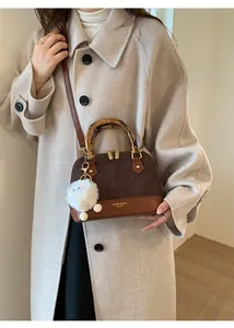 Detail of vintage shell bag featuring bamboo handles and a plush white charm on a brown body