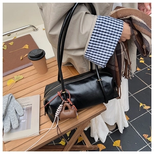 Detail of a black glossy leather cylinder bag with a mini brown charm on a wooden table