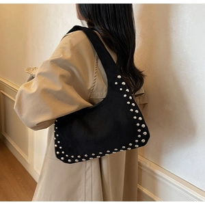 Detail of black underarm bag with silver studs worn by model in urban casual style