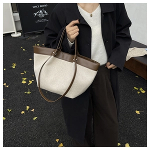 Chic beige canvas and brown leather tote bag held by a model on a scenic street