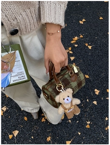 Close-up of green plaid Boston bag featuring a plush teddy bear charm and leather handle