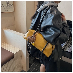 Detail of yellow leather hobo bag featuring slim black straps and a mini bag charm pendant