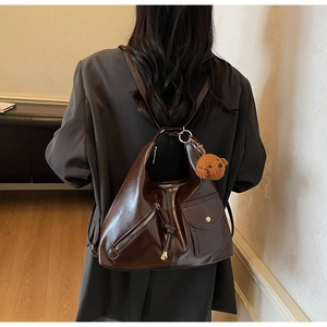 Detail of dark brown leather hobo bag featuring external zip pocket and plush bear charm