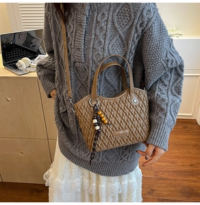 Detail of a brown woven bucket bag with wood bead charm and adjustable shoulder strap