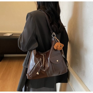 Detail view of large dark brown leather tote bag with a small bear pendant on shoulder strap
