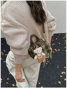 Detail of checkered woolen Boston bag with cute teddy bear charm on autumn background