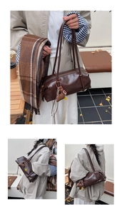 Detail of dark brown glossy barrel bag paired with a plaid tassel scarf in autumn setting