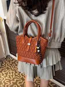 Brown woven texture handbag with shoulder strap and decorative bead pendant on a model