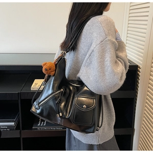Detail of multi-pocket black leather tote bag with fringes and a bear pendant on model