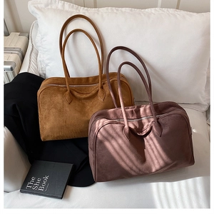 Detail of large suede tote bags in tan and mauve on a bed with a black blazer