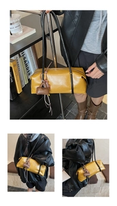Detail of yellow rectangular shoulder bag with slim black handles and mini charm