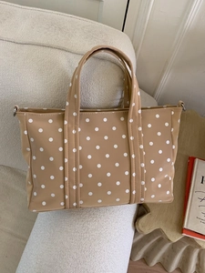 Beige polka dot tote bag with top handles on a sofa in a minimalist fashion scene