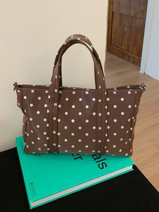 Brown polka dot tote bag with leather straps displayed on a book in a home setting