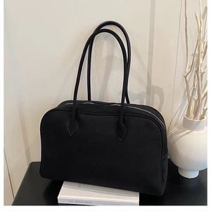 Detail view of black faux suede Boston bag with long handles on a minimalist table