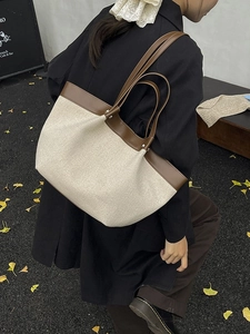 Canvas and brown leather tote bag with a wing-shaped design shown on a shoulder