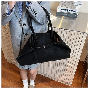 Macro detail of black suede tote bag featuring a metallic buckle and long leather tassel