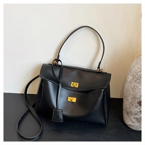 Detail of minimalist black leather tote bag with gold twist locks on dark wood surface