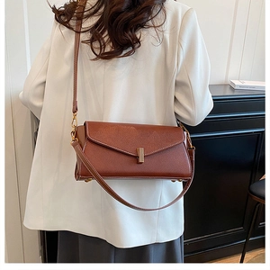 Sac bandoulière en cuir marron avec détails dorés porté par un mannequin en costume