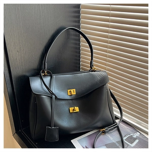 Detailed close-up of a matte black leather handbag with a golden rotating clasp and metal charm